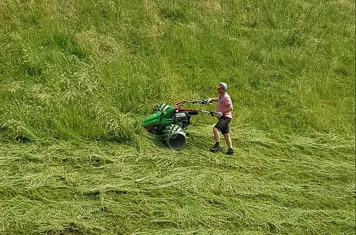 Gastgeber und Bauer Herbert mäht das Gras auf unseren steilen Bergwiesen mit der Stachelwalzen-Mähmaschine.